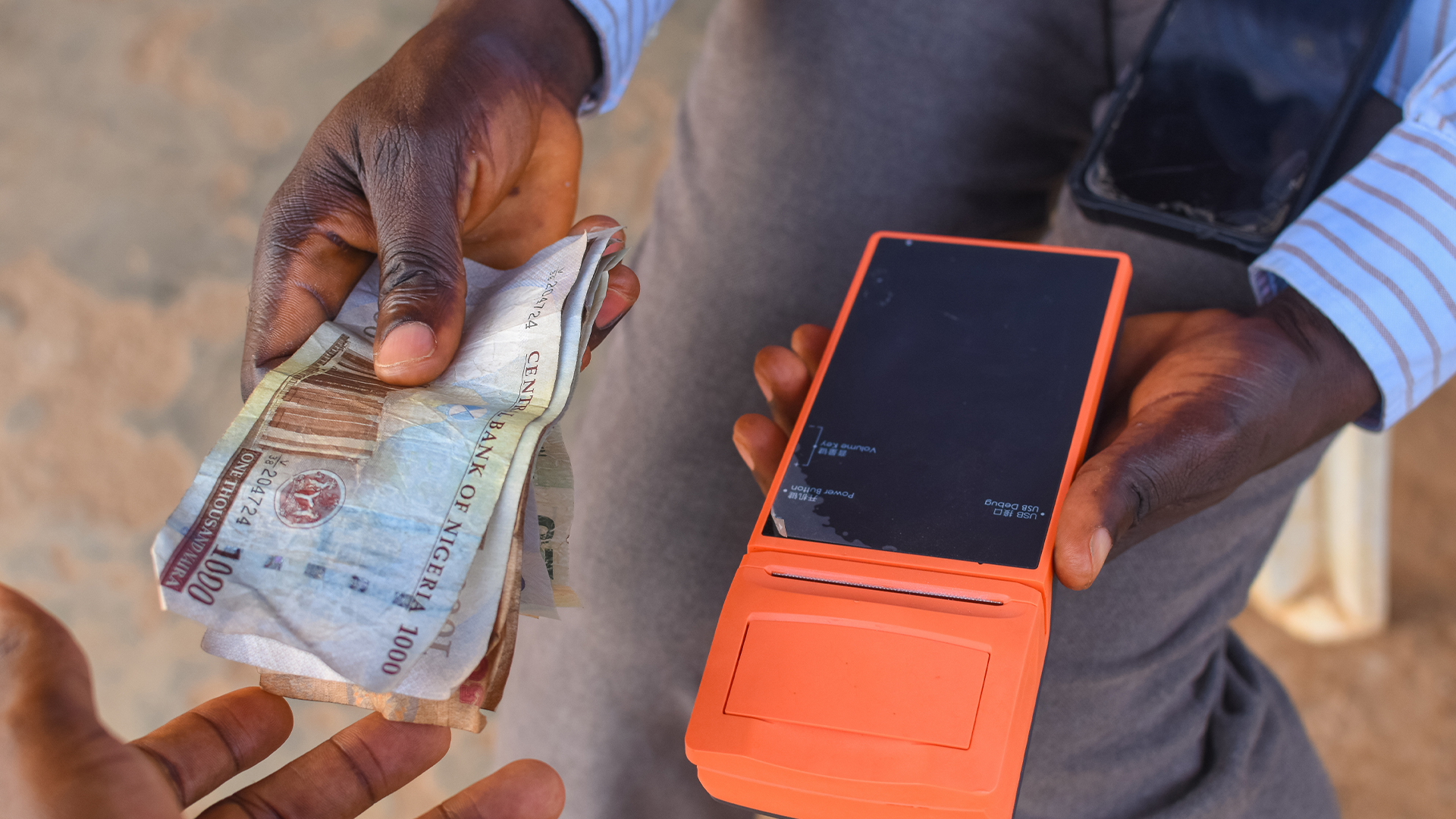 Hands of two african individuals doing financial transaction with a point of sales POS terminal as Cash, Naira, Money or currency is exchanging hands